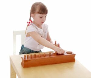 A child concentrating on a practical life task, using a small broom and dustpan to clean up.